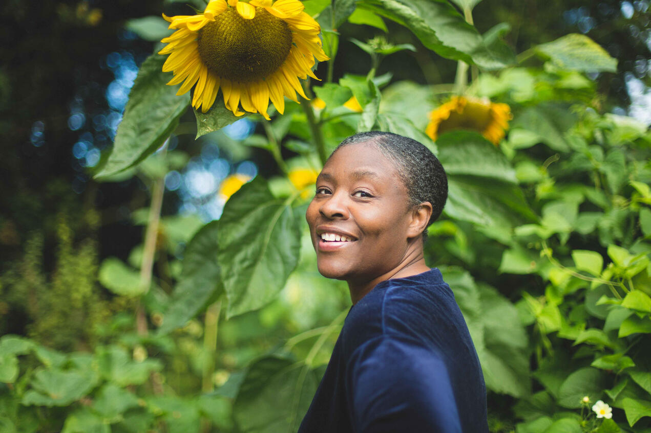 Personal branding photo of a life coach in Lincolnshire garden, smiling back at the camera with a sunflower in frame.