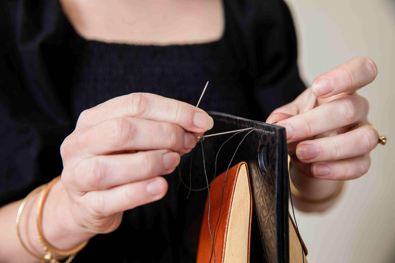 Close-up detail: leather maker sewing a handbag in her workshop.