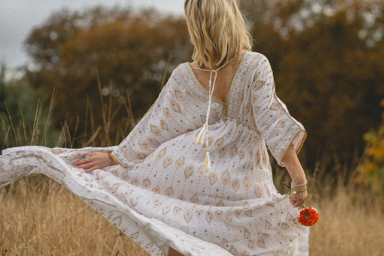 Personal branding photo of a movement practitioner in nature, flowing dress and flower in hand during a chakra dance practice.