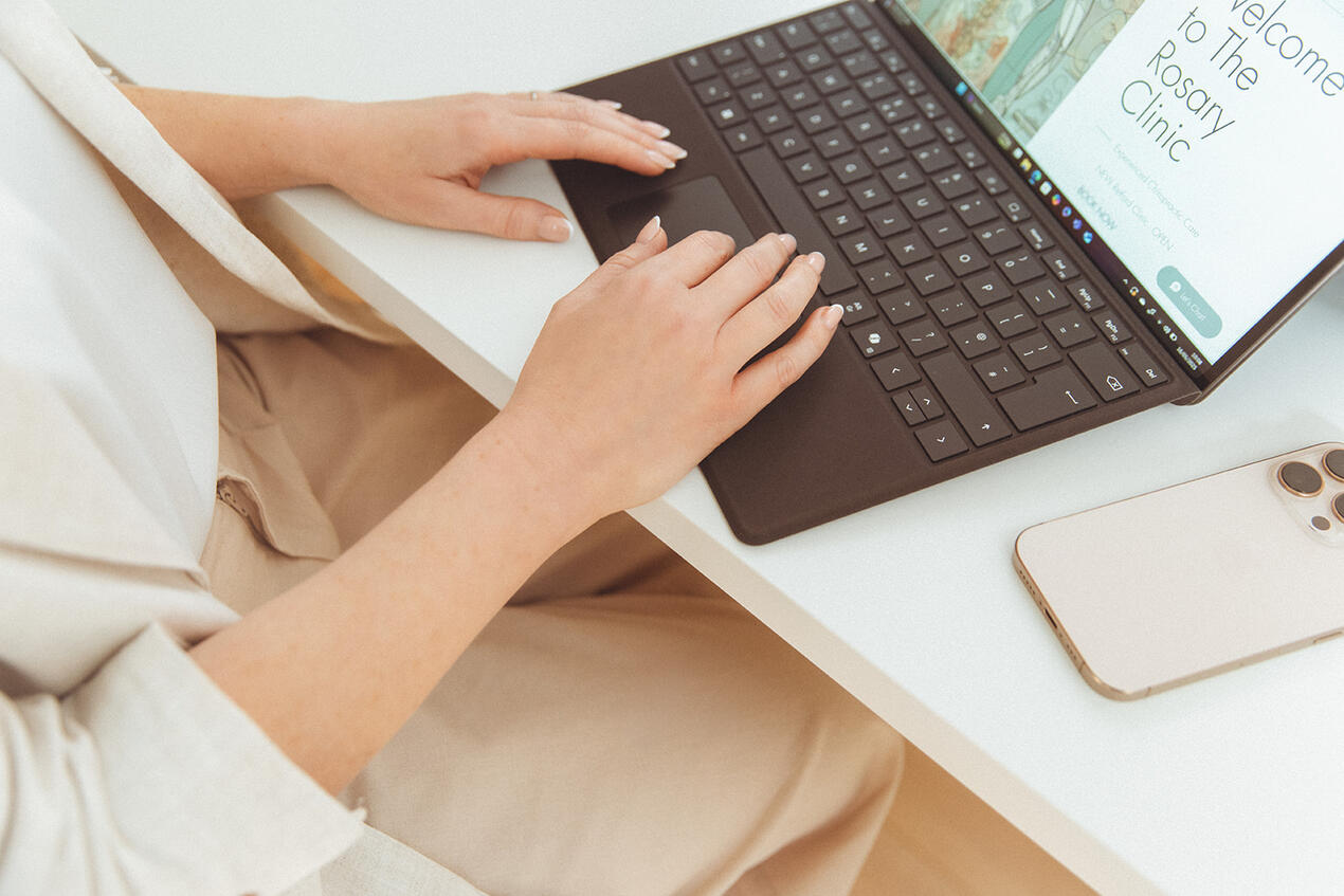 Close-up brand photo of a chiropractor’s hands typing on her laptop.